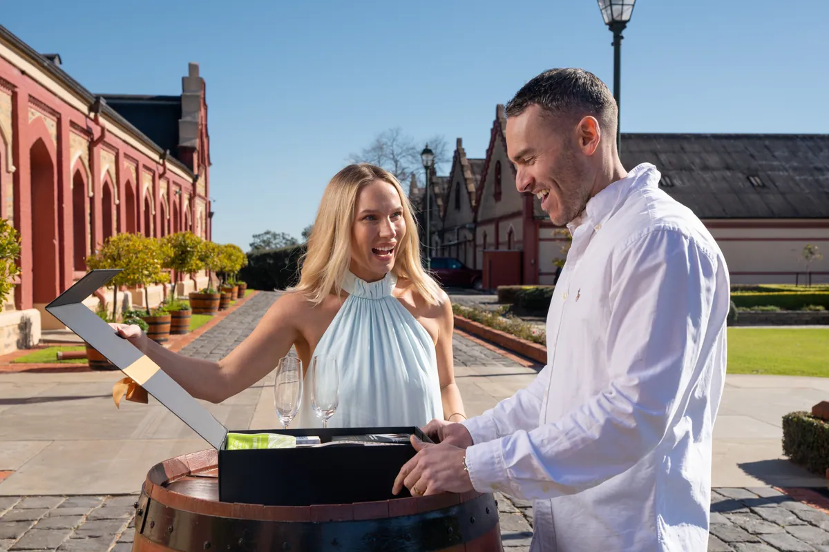 A couple opening a Father's Day gift hamper on a wine barrel at a Barossa Valley winery